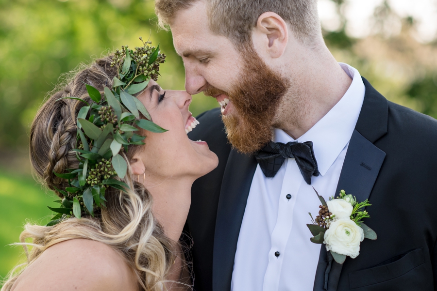 A bride in a flower crown and groom in a tux laughing.